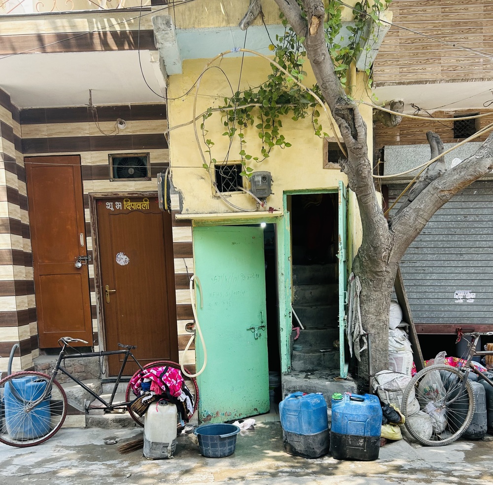 An image of two houses taken during fieldwork in Delhi, with trees, bicycles and containers outside the homes.