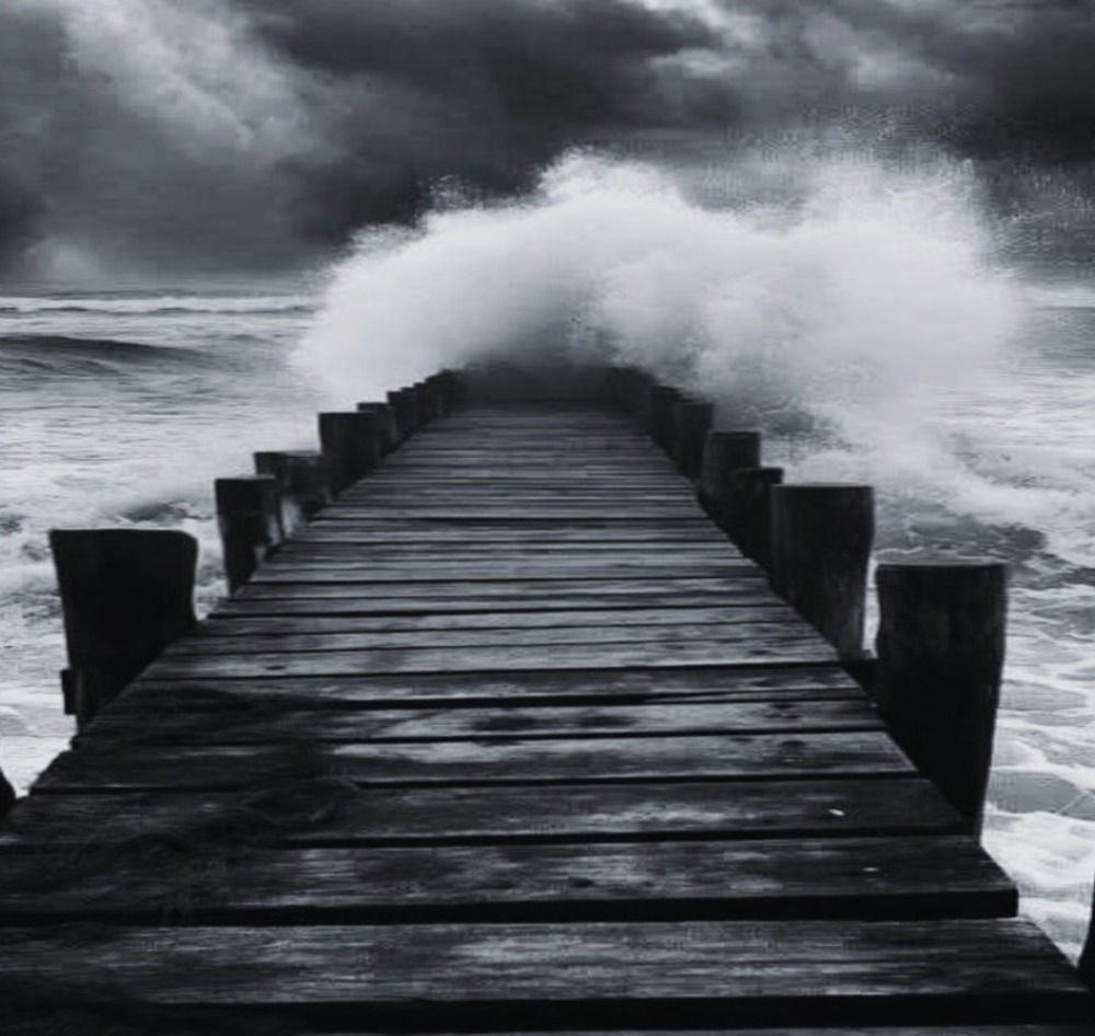 A wooden bridge out to sea ends with a swirl of waves and foam