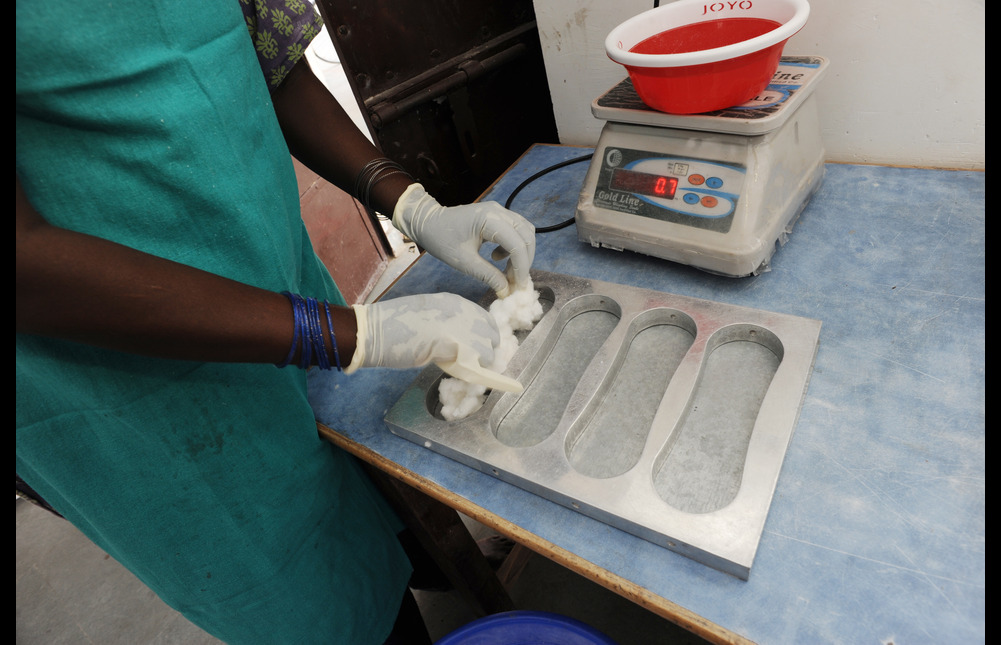 A person placing pulverised cotton into a sanitary pad mould.