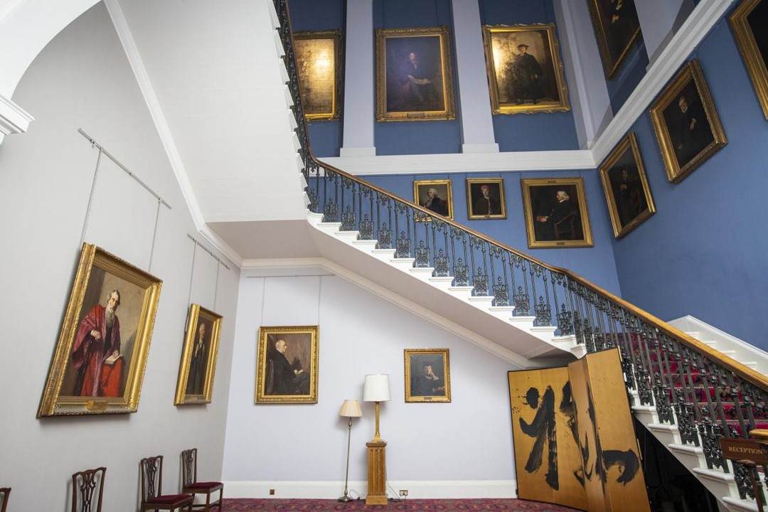 Old college stairwell featuring portraits of s filled with portraits of former professors, principals and famed thinkers, almost exclusively white old men.