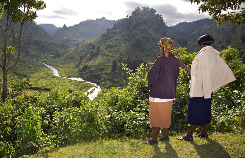 Two women looking out over a natural area with hills, grass and a stream.