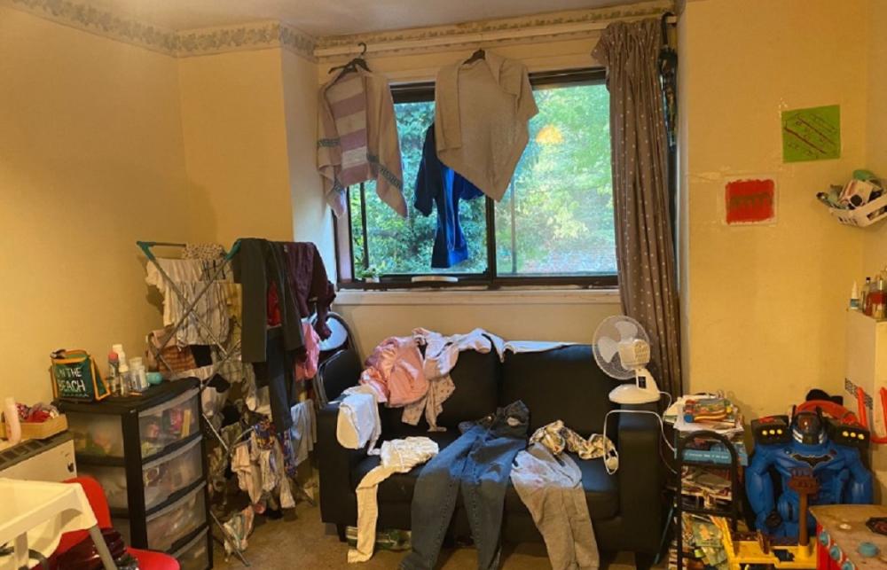 A photo of Rayan's sofa. Clothes have been laid on it to dry, and more clothes are hanging over it. 