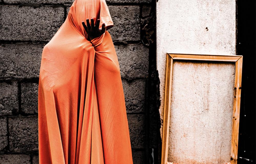 A red hooded figure stands next to an empty picture frame