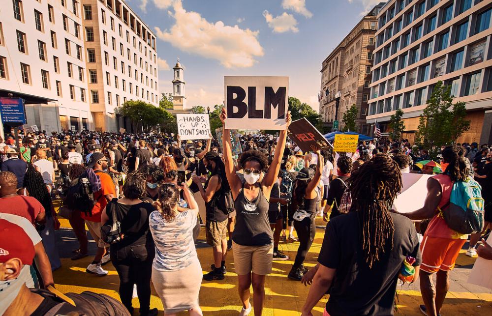 A masked member of a crowd holds up a BLM sign