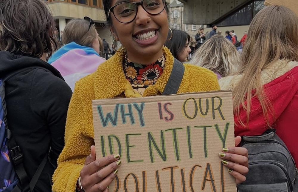 an image of Sharessa holding a protest sign that reads "Why is our identity political"