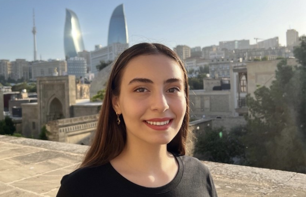 A picture of Sara in front of a city, she wears a black top