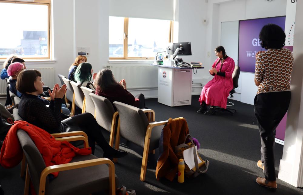 Picture of GENDER.ED's welcome reception where the feminist trailblazer awards were awarded. It shows poet Nadine Aisha Jassat sitting on a chair after reading out her poetry in front of two rows of people sat on chairs.  