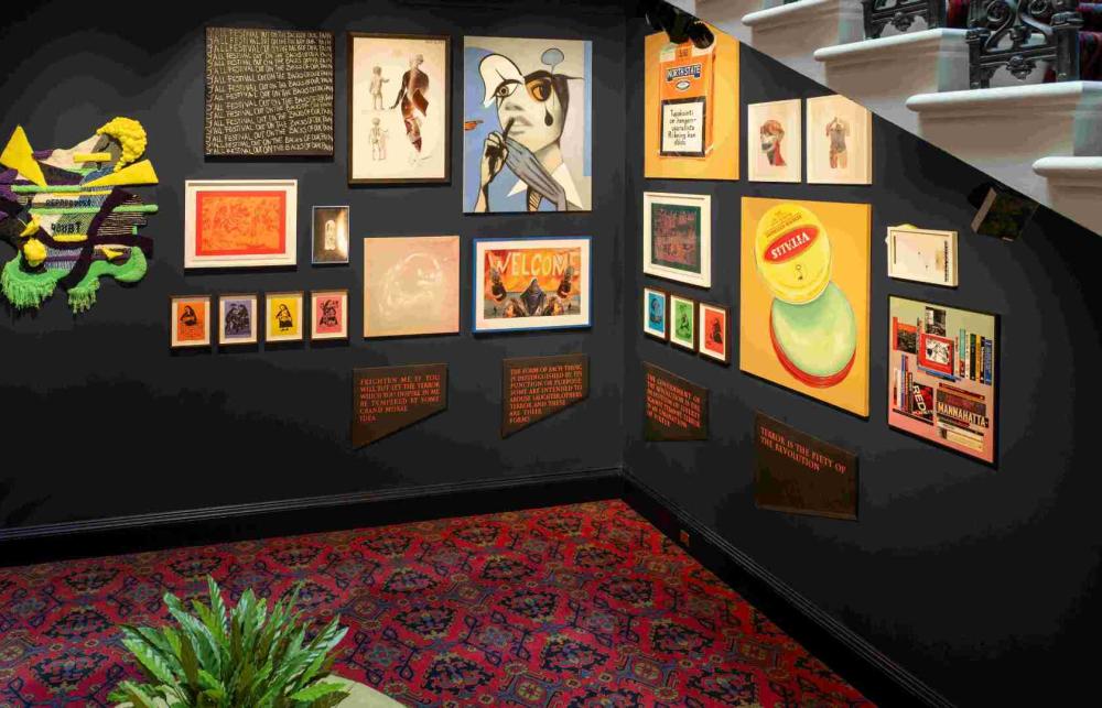 Display of art works at the Old College of the University of Edinburgh. The display is located below a staircase and consists of a variety of vibrant and colourful pieces. There is a plant across the artwork. 