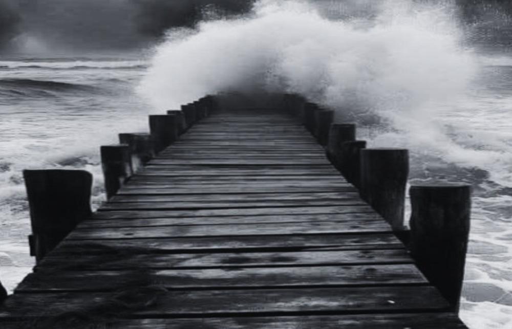 A wooden bridge out to sea ends with a swirl of waves and foam