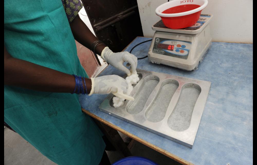 A person placing pulverised cotton into a sanitary pad mould.