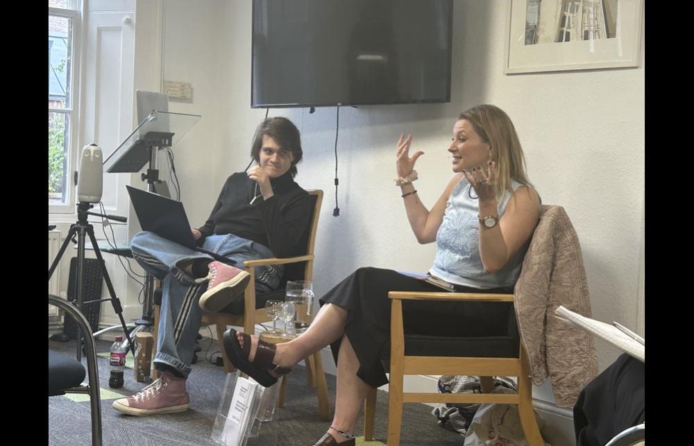 Image of Helen Shutt gesticulating in a lively way, in conversation with Jack MacGregor at the front of the IASH meeting room